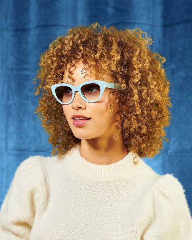 Lady with curly hair wearing Garrett Leight Dottie sunglasses in powder blue
